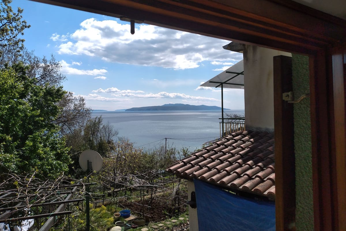A view from a balcony overlooking a body of water with distant mountains, a satellite dish, and a tiled roof.