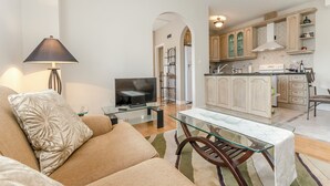 A living room with a sofa, a glass coffee table, and a TV. There is a kitchen with cabinets and a dining area with a table and chairs. - Apartment Canada Dream Vacation (Srima)