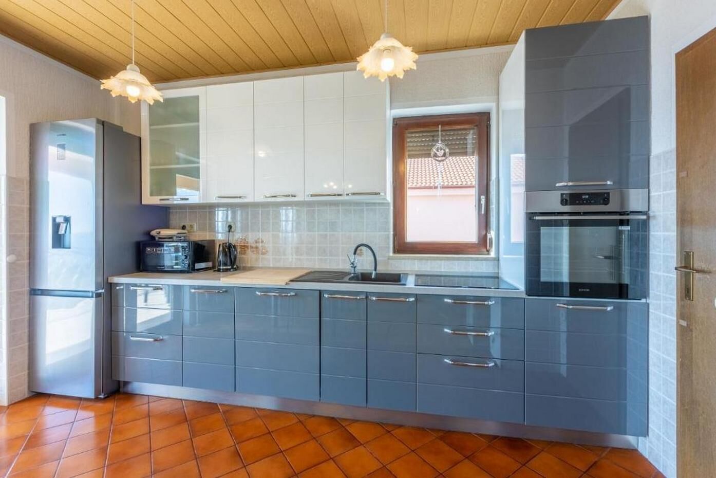 A modern kitchen with grey cabinets, a built-in oven, and a refrigerator.