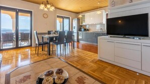 Un grand espace de vie comprenant une table à manger, des chaises, un téléviseur et une cuisine à l’arrière-plan.