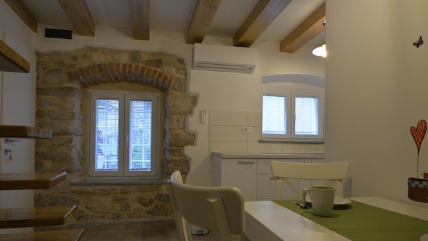 Una cucina con arco in pietra, travi in legno, un piano di lavoro bianco e una finestra con persiane.