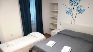 Una camera d'albergo con un letto matrimoniale, un letto singolo, un armadio e un muro decorato con un affresco di alberi e farfalle.