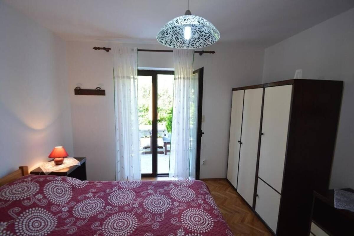 A bedroom with a bed, a nightstand, a wardrobe, and a door leading to an outdoor area.