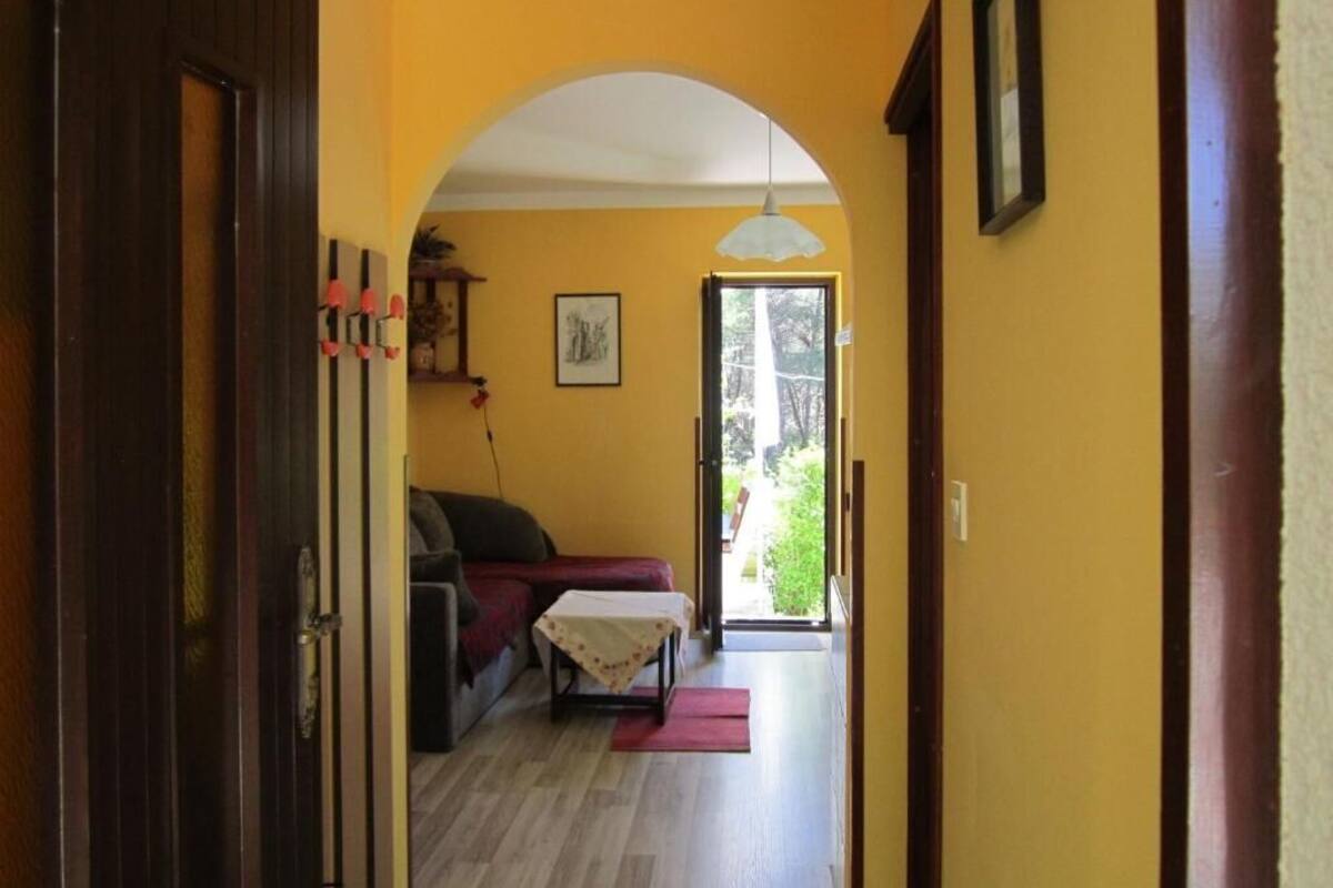 A hallway with a wooden door, a couch, a small table, and a doorway leading to an outdoor area.