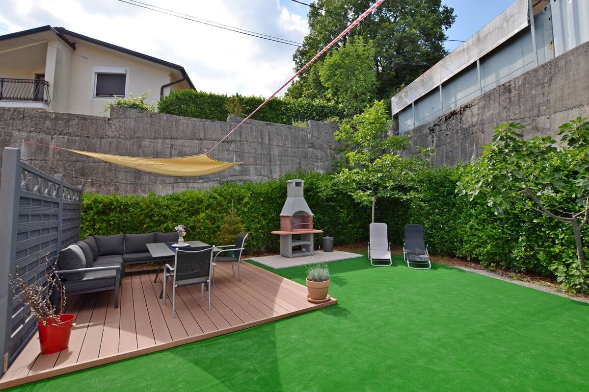 Un giardino con un patio in legno, un barbecue, un divano e due poltrone.