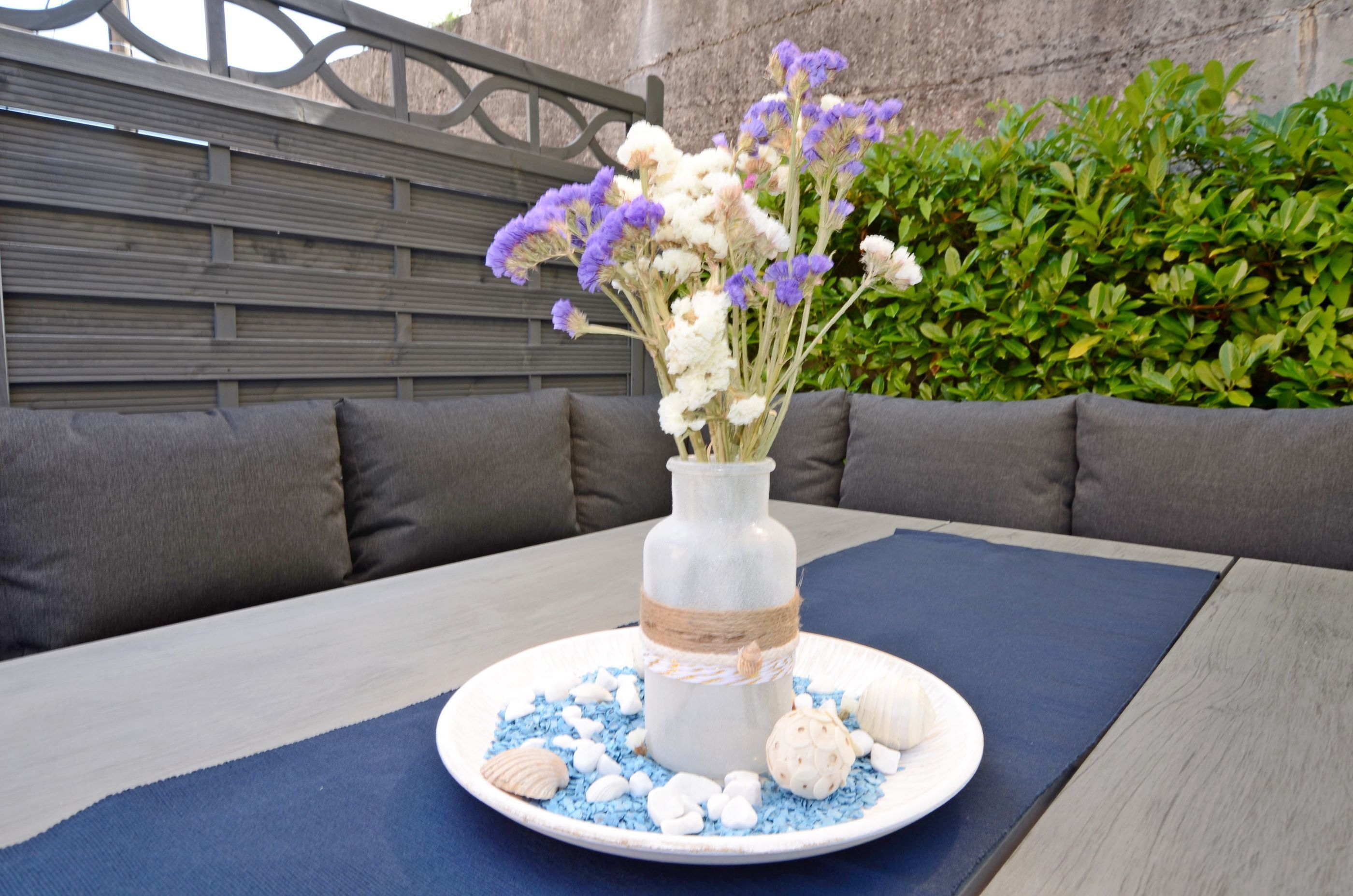 A table with a vase of flowers, a plate with seashells, and a blue placemat.