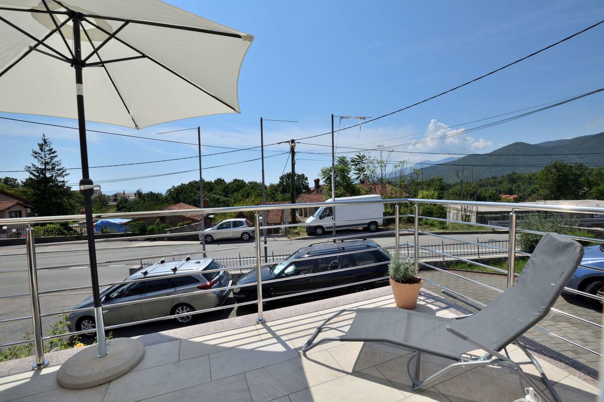 Un balcone con una poltrona da relax, una pianta in vaso e un ombrellone grande.