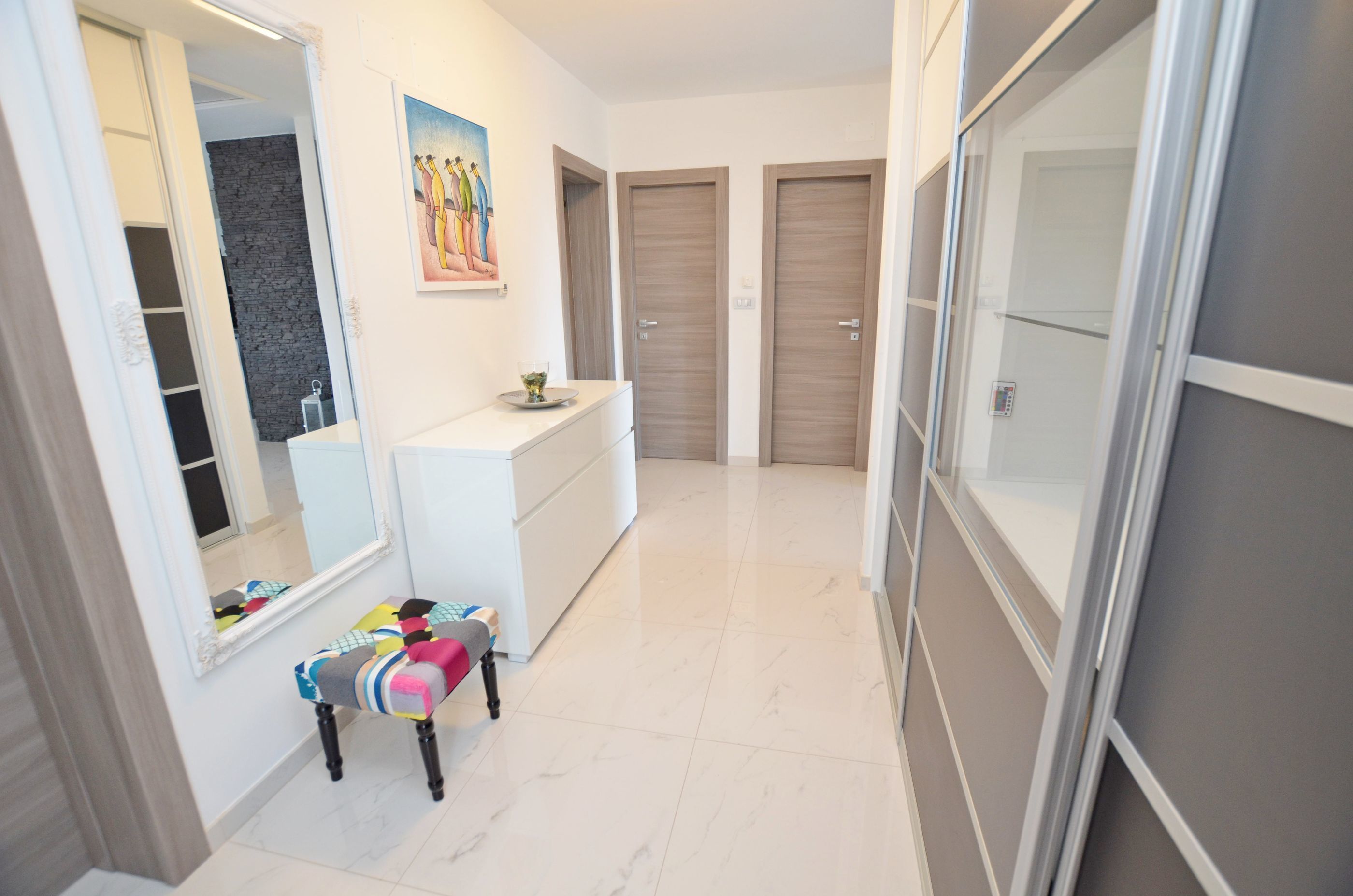 A hallway with a white bench, a large mirror, a painting, and two wooden doors.
