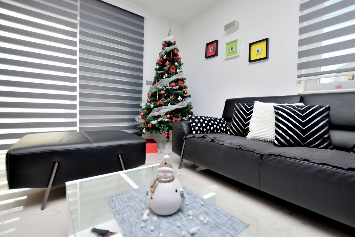 Un soggiorno moderno con un divano nero, un tavolino in vetro e un albero di Natale.