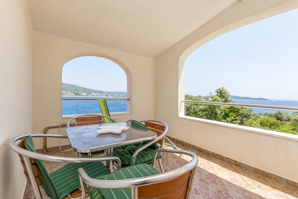 A balcony with a table and chairs, a view of the sea, and a stone floor.