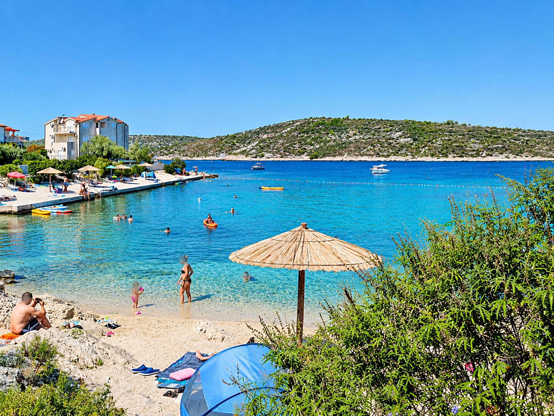 A beach with clear blue water, a sandy shore, and a few umbrellas.