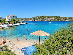 A beach with clear blue water, a sandy shore, and a few umbrellas. - Apartments Bozo (Kanica)