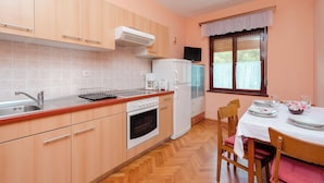 Cozinha com armários de madeira, forno embutido, geladeira e mesa de jantar posta para dois, com cadeiras.