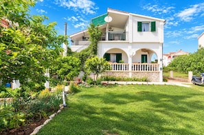 A two-story building with a balcony, surrounded by a well-maintained garden and a clear blue sky. - Apartments Sunset Beach (Vodice)