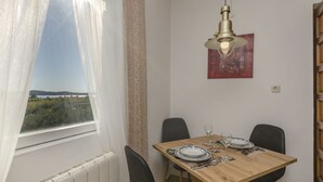 Un comedor con una mesa de madera, sillas negras, una lámpara colgante y vistas a la vegetación a través de una ventana.