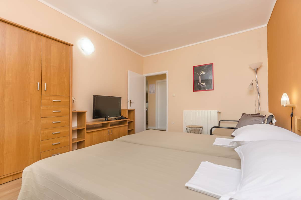 Ein Schlafzimmer mit einem Bett, einem Holzschrank, einem Fernseher, einem Nachttisch, einer Lampe und einer Tür zu einem weiteren Raum.