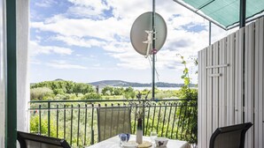 Un balcón con una mesa dispuesta para dos personas, una antena parabólica y vistas a zonas verdes y colinas.
