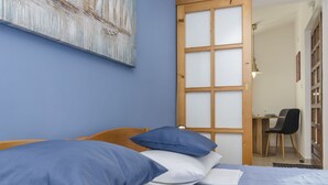 Un dormitorio con cama, almohadas azules y blancas, cabecera de madera, un escritorio con silla y un cuadro en la pared.