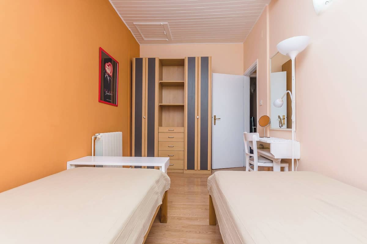 Ein Schlafzimmer mit zwei Betten, einem Schreibtisch mit Stuhl, einem Kleiderschrank und einem Badezimmerspiegel.