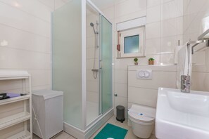 A modern bathroom with a glass-enclosed shower, a white sink, and a small potted plant on the vanity. - Apartment Adrian (Omis)