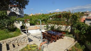 An outdoor patio with a stone wall, a grill, and a wooden table and bench. - Apartments Marlen (Mali Losinj)
