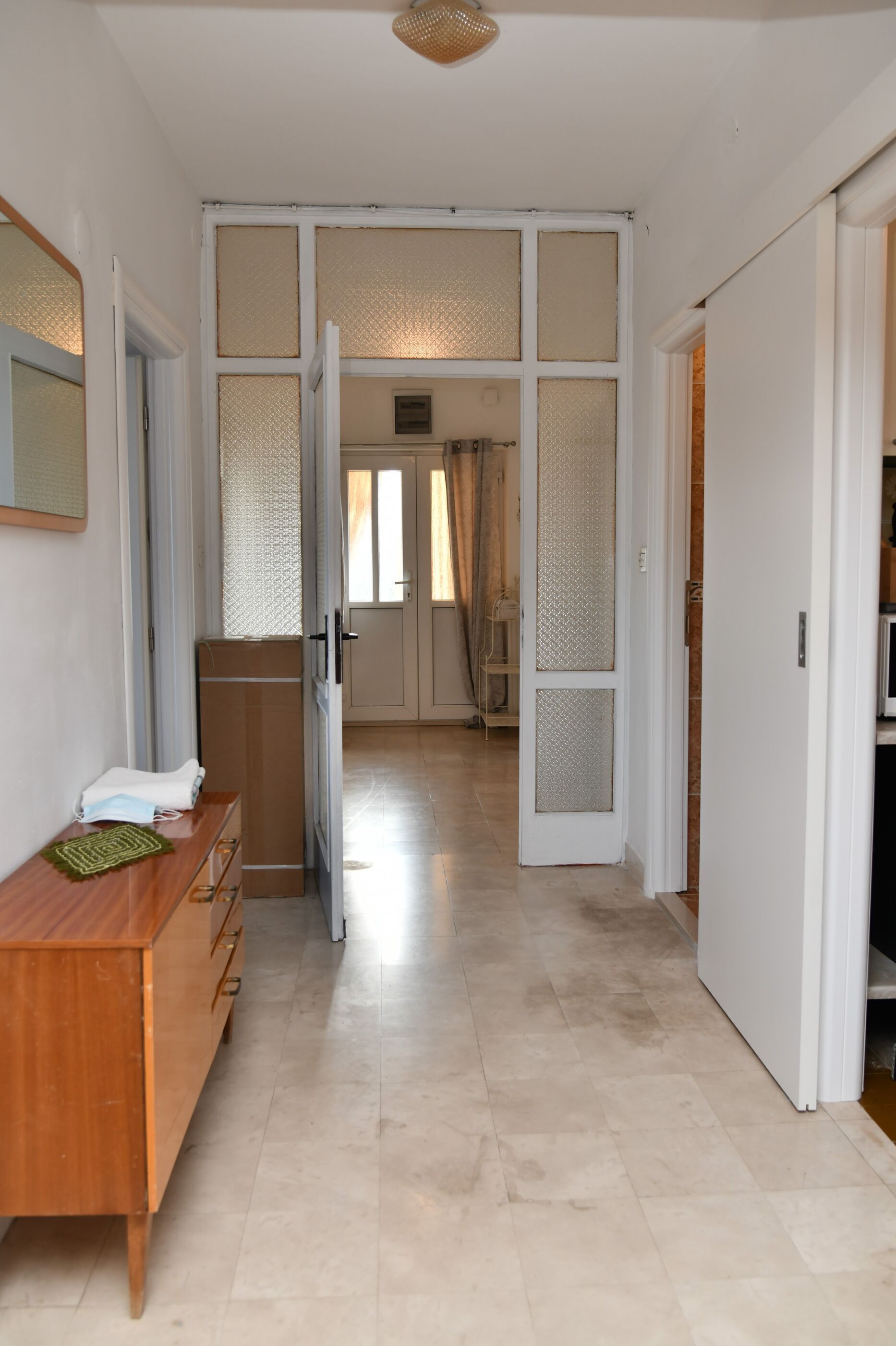 A hallway with a wooden dresser, a mirror, and a door leading to another room.