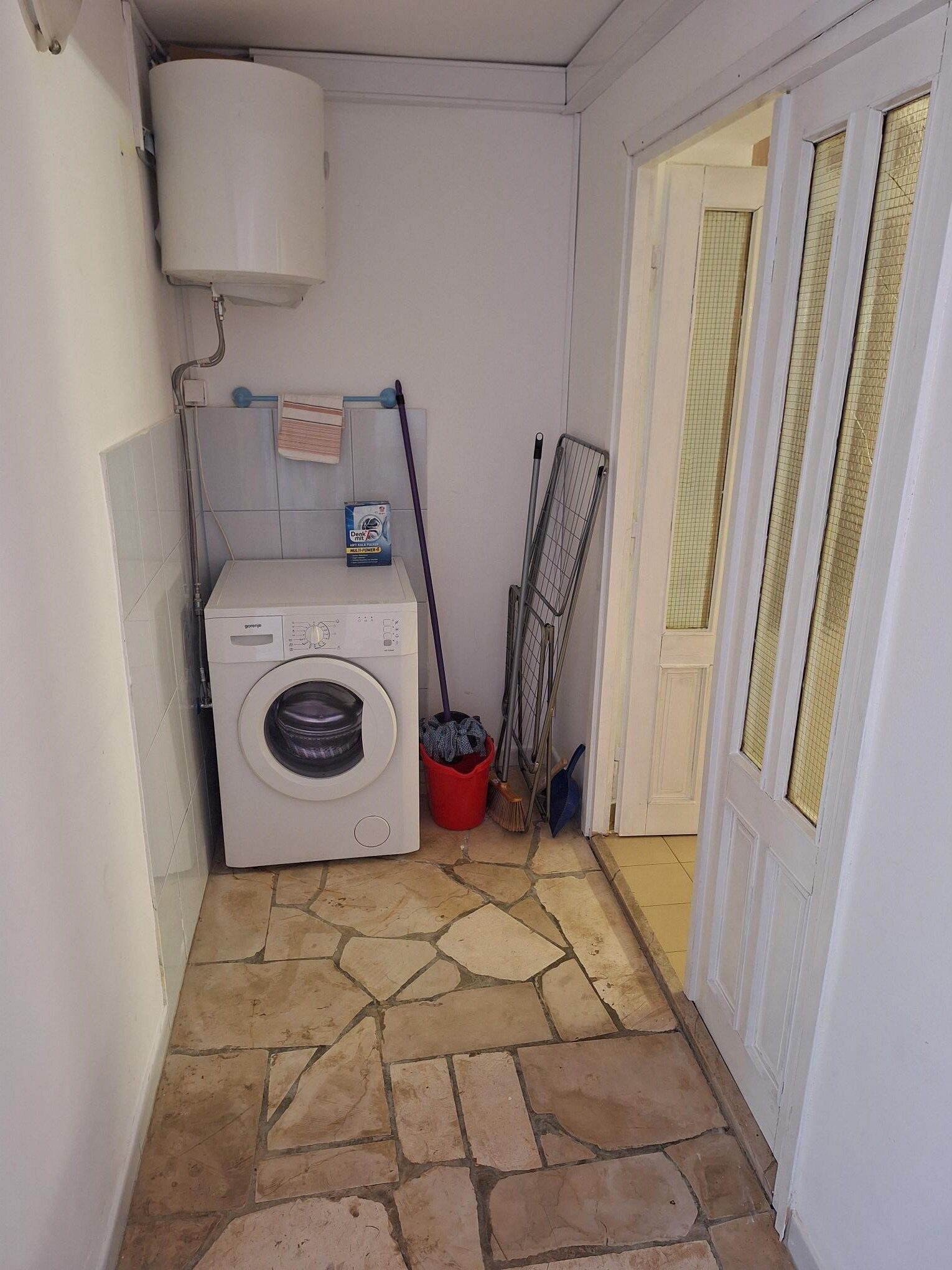 A laundry area with a washing machine, a bucket, and cleaning tools.