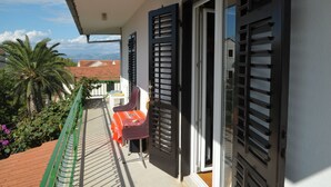 A balcony with a table and chairs, a door, and a view of palm trees and buildings. - Apartments Valerija (Supetar)