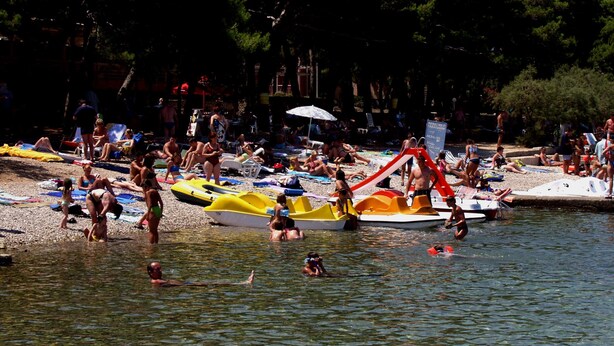A crowded beach with people sunbathing and swimming, and several small boats on the shore. - Apartments Valerija (Supetar)