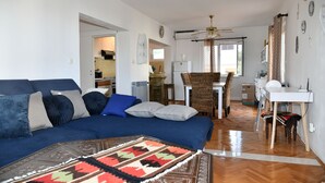 A living room with a blue sofa, a patterned rug, a dining table with chairs, and a kitchen in the background. - Apartments Valerija (Supetar)