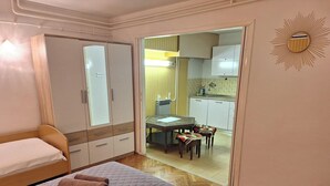 A bedroom with a bed, a wardrobe, and a view into a kitchen area. - Apartments Valerija (Supetar)