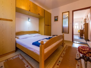 A wooden bed with a headboard, a bedside table, and a nightstand. There is a mirror on the wall and a door leading to another room. - Apartments Dubravka (Crikvenica)