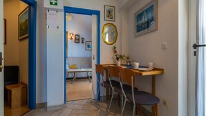 A hotel room with a dining area featuring a wooden table, two chairs, and a small table with a vase of flowers. - Apartments Dubravka (Crikvenica)