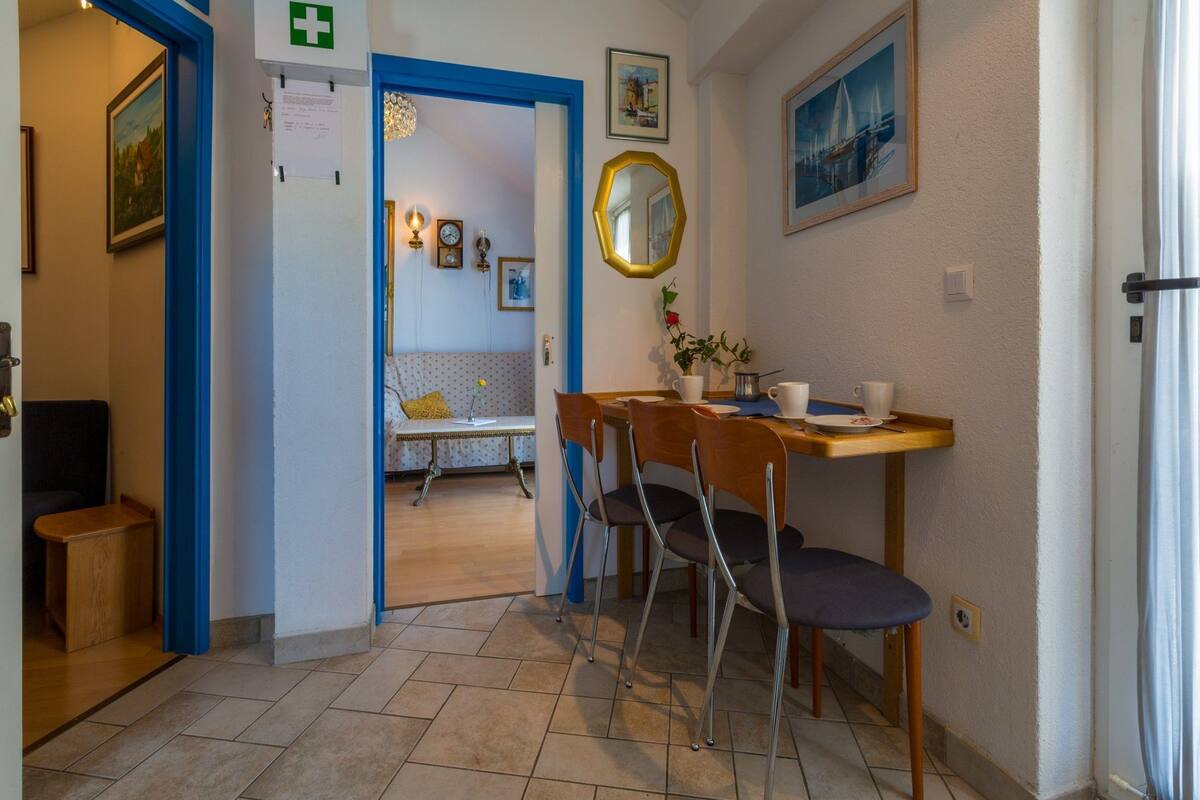 Ein Hotelzimmer mit einem Essbereich, der einen Holztisch, zwei Stühle und einen kleinen Tisch mit Blumenvase umfasst.