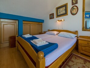 A double bed with blue and white bedding, wooden headboard, and a nightstand with a mirror. - Apartments Dubravka (Krk)