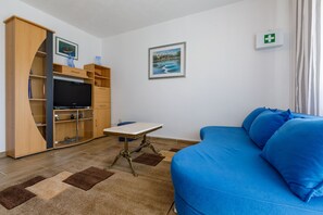 A living room with a blue sofa, wooden entertainment unit, TV, and a small table. - Apartments Dubravka (Crikvenica)