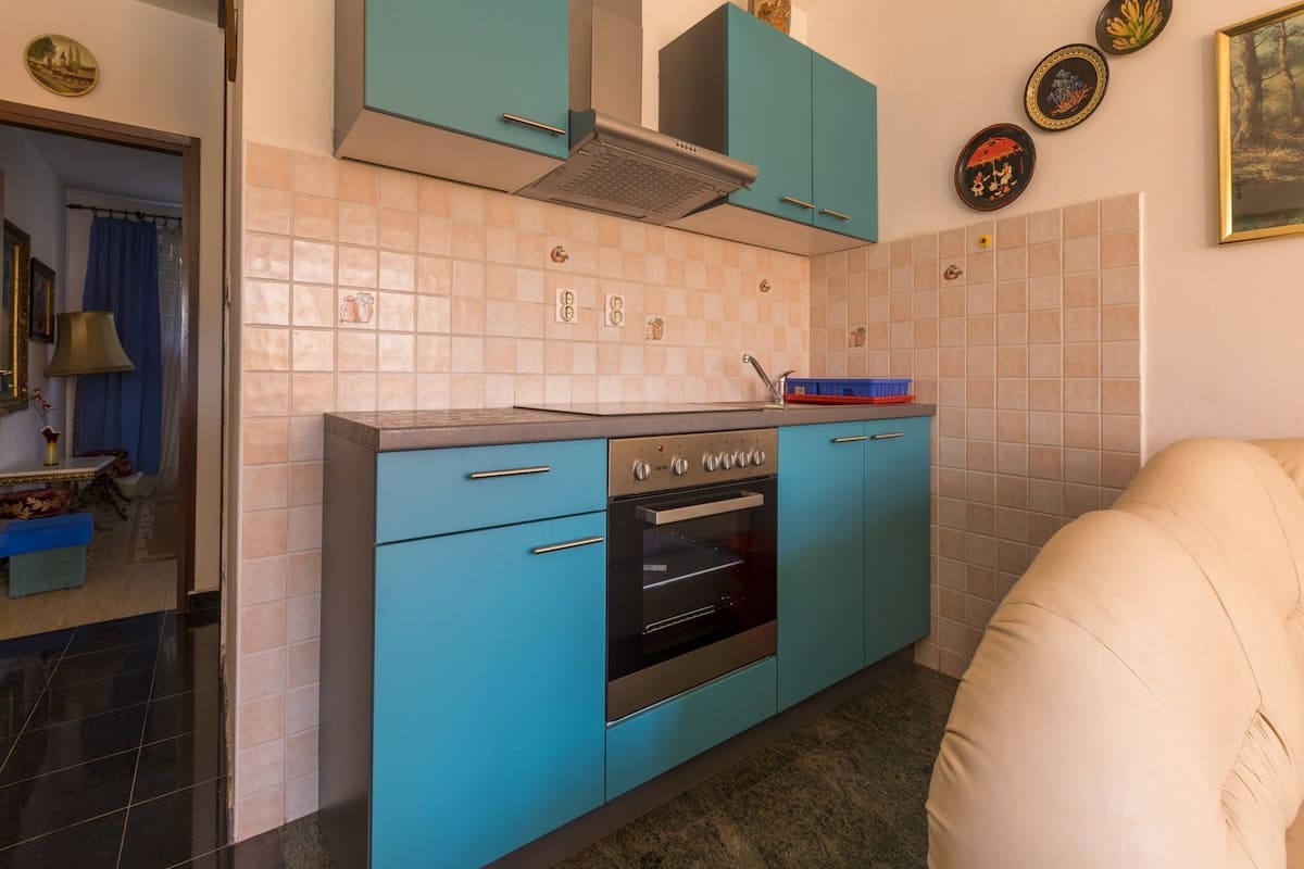 Eine kleine Küche mit türkisfarbenen Schränken, einem eingebauten Backofen und einer gefliesten Spritzschutzwand.