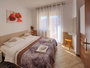 Habitación de hotel con una cama grande, una mesita pequeña, una silla, un espejo y una ventana con cortinas.