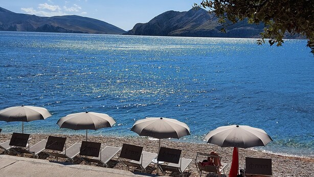 Vista panorámica de un lago con aguas azules cristalinas, una fila de sillas de playa y sombrillas.