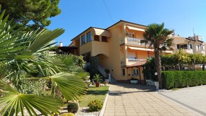 Un edificio de varios pisos con balcones, un camino pavimentado y vegetación circundante.