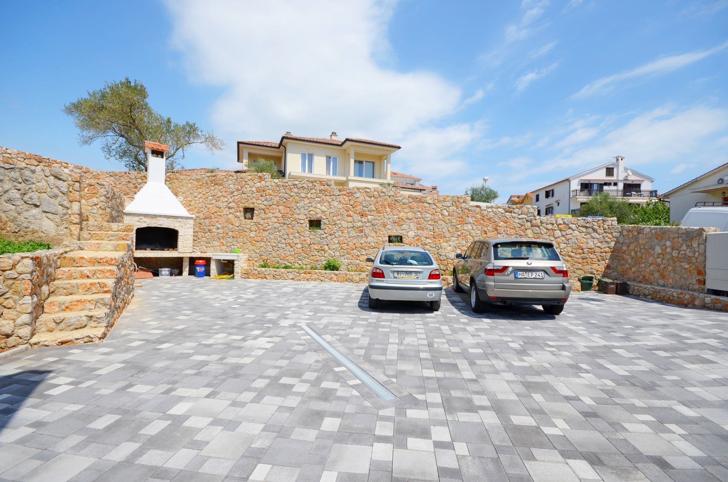 A stone-walled building with a paved driveway, two parked cars, and a chimney.