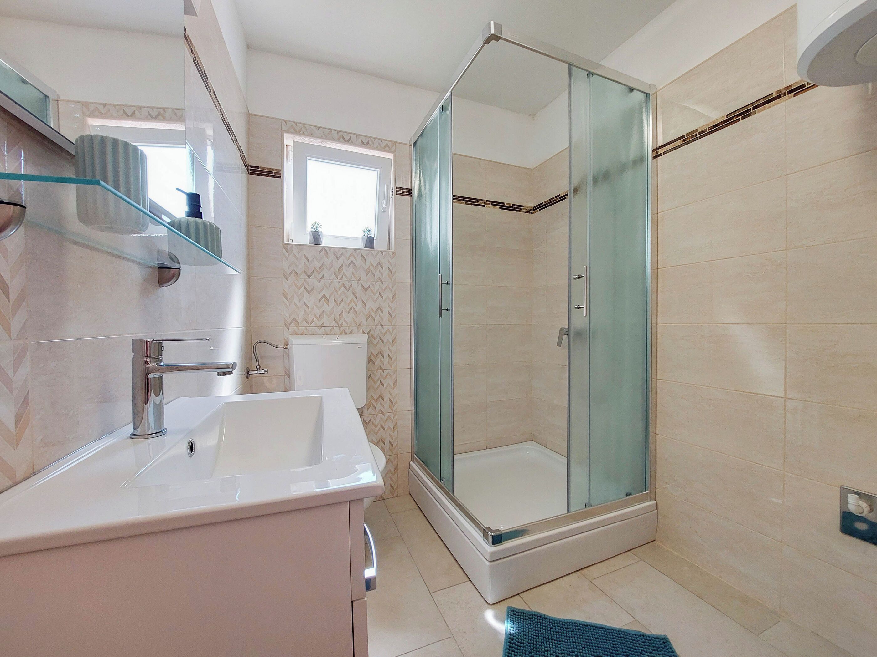 Een moderne badkamer met een douchecabine van glas, een witte wastafel en een toilet.