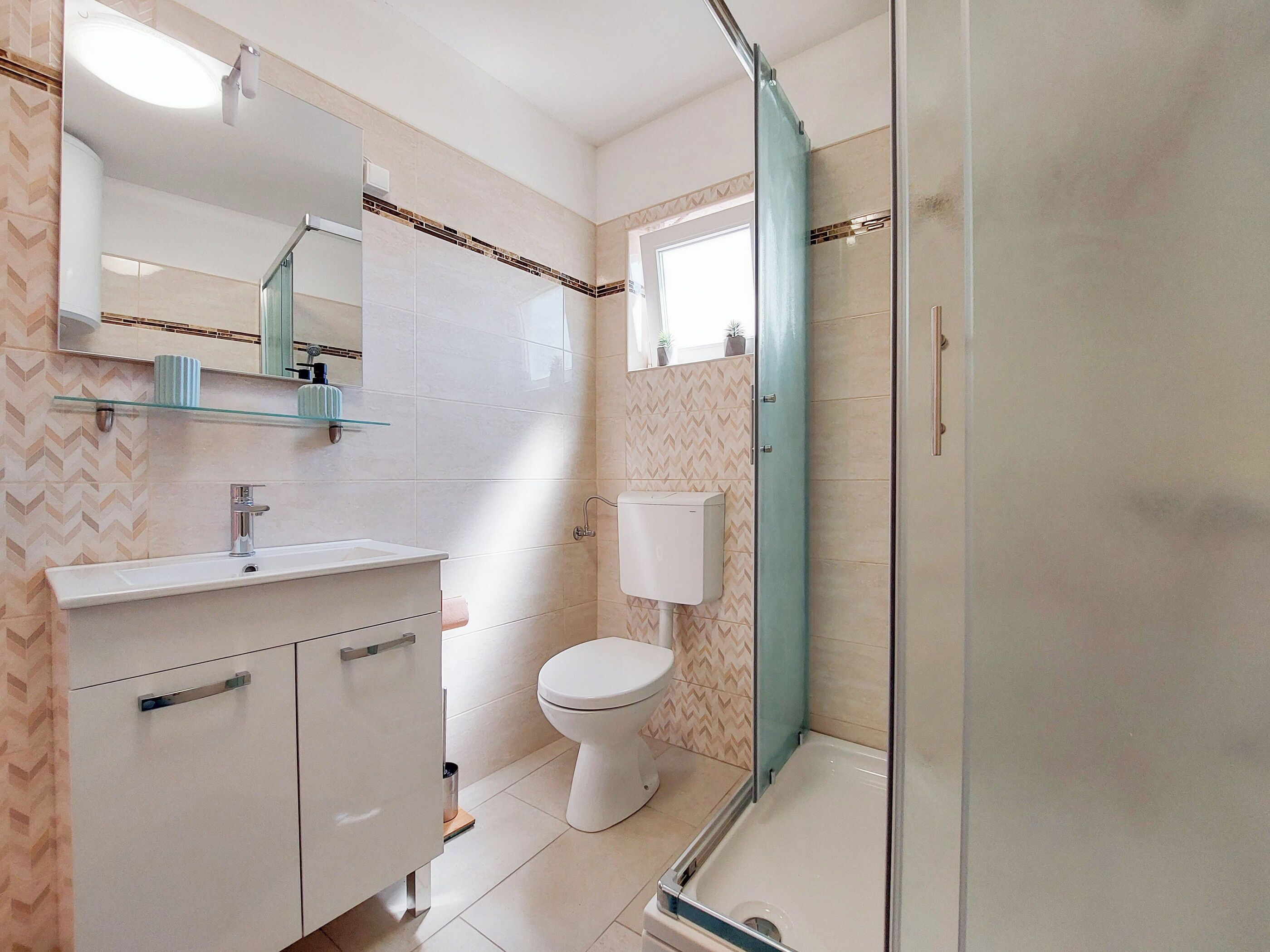 A modern bathroom with a glass shower enclosure, a white toilet, and a vanity with a mirror and shelf.