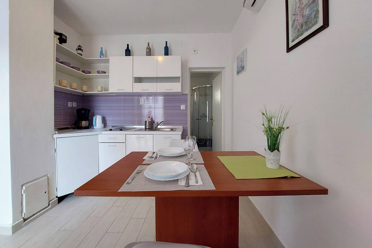 Una cocina moderna con armarios blancos, salpicadero morado y comedor con mesa de madera dispuesta para dos personas.