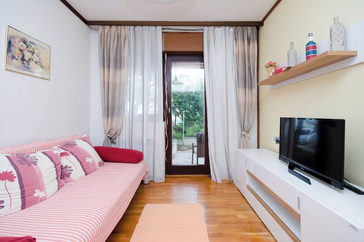 Una sala de estar con sofá, televisión y vistas a través de una puerta.