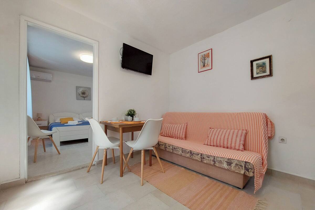 Un espacio habitable compacto con comedor, un sofá y un televisor fijado a la pared.
