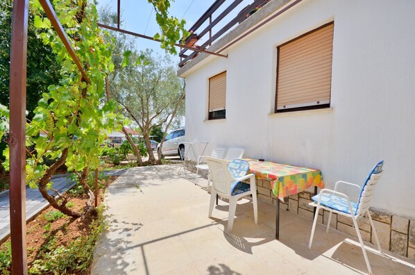 A patio with a table and chairs, a white wall, and a vine-covered trellis. - Apartments Ivanka (Krk)