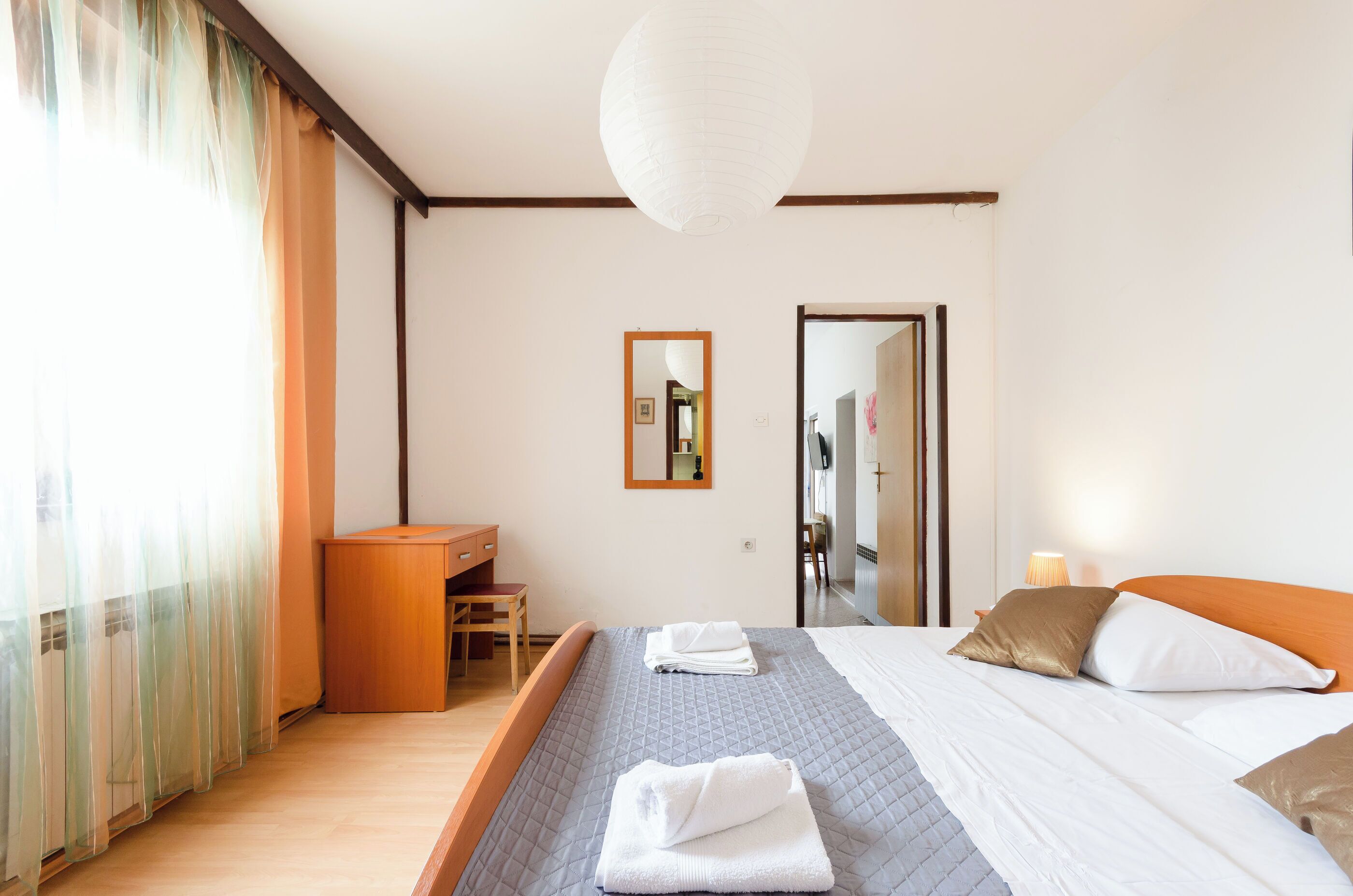 A hotel room with a bed, a desk, a chair, and a mirror.