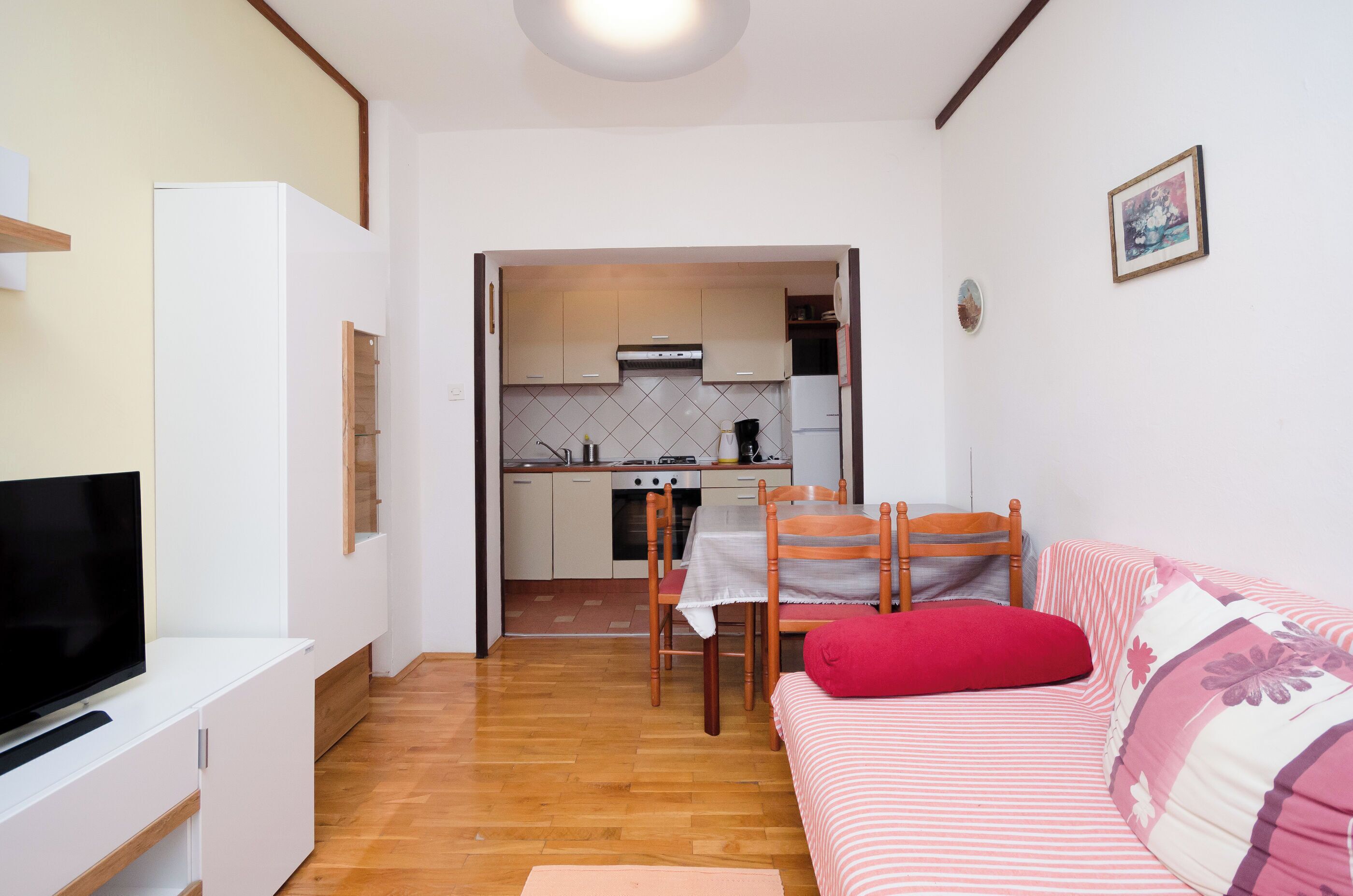 Een compacte woonruimte met een kitchenette, een eethoek en een bank met een rood kussen.