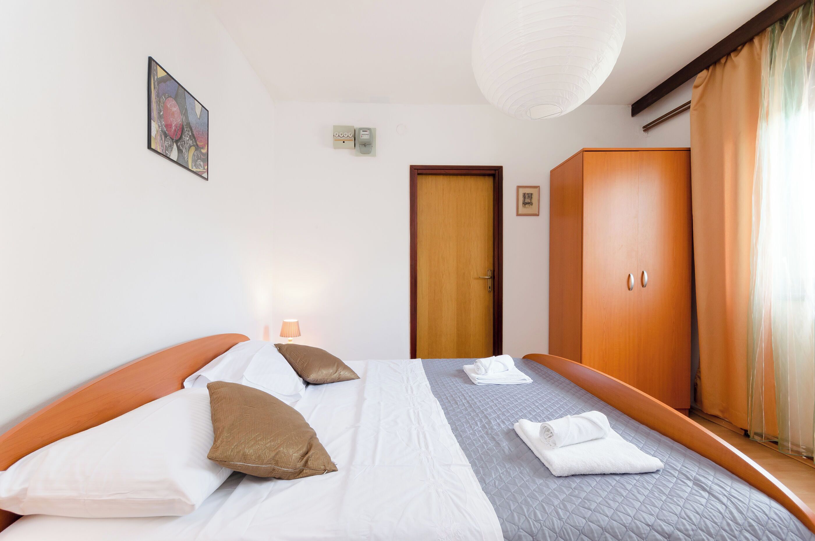 A hotel room with a bed, a wardrobe, a door, and a painting on the wall.